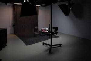 An image of the production studio with photo backgrounds unrolled, a stool, camera and laptop set up for taking portraits.